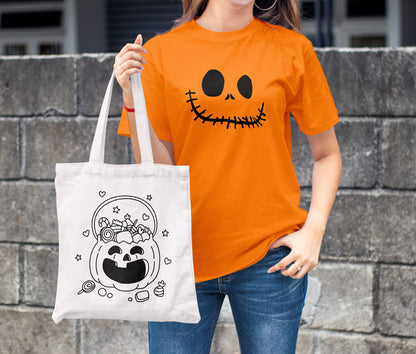 Frau in orangefarbenem T-Shirt mit "Monster Face" hält eine Baumwolltasche mit Kürbis-Motiv in der Hand.