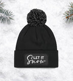 Schwarze Bommelmütze mit dem Aufdruck "Let It Snow" – perfekt für winterliche Tage und festliche Stimmung.