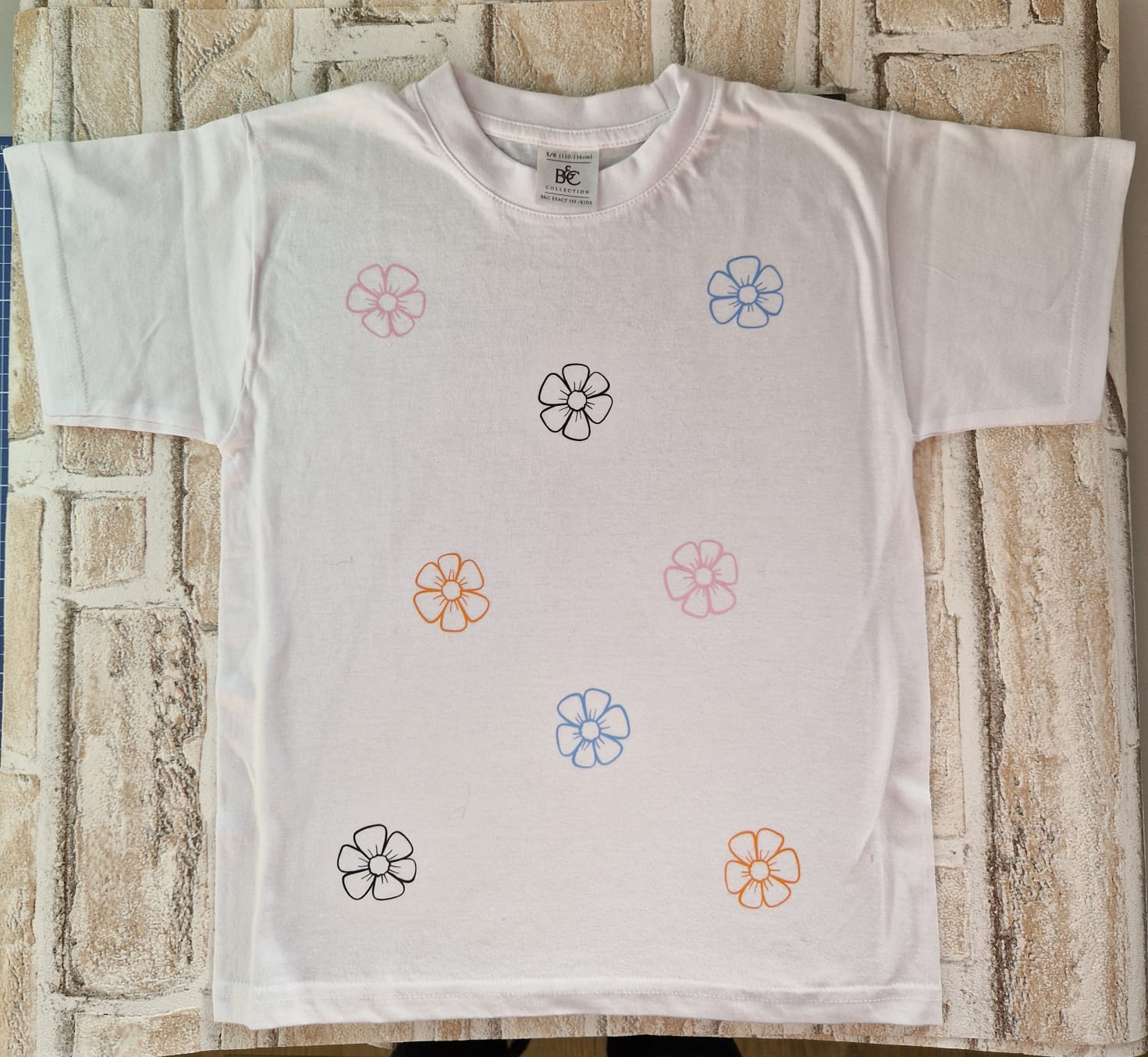 Bunt bedrucktes weißes T-Shirt mit floralen Designs, perfekt für einen frischen, kreativen Look.